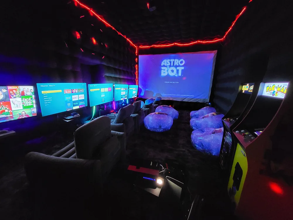 Gaming lounge with multiple TV screens and arcade machines at Backyard Movie Theater